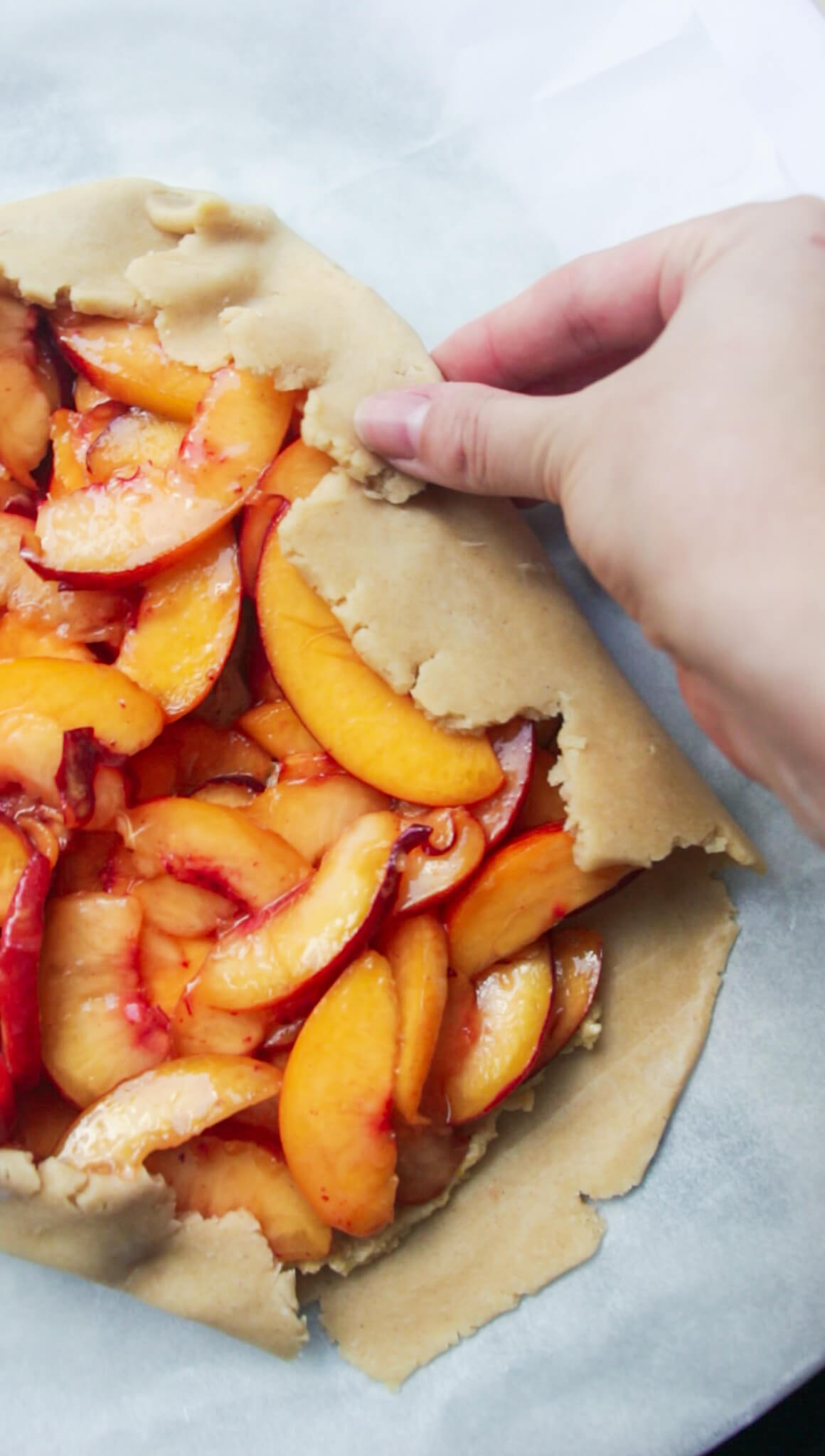 Hand folding pastry over peaches to form a galette.