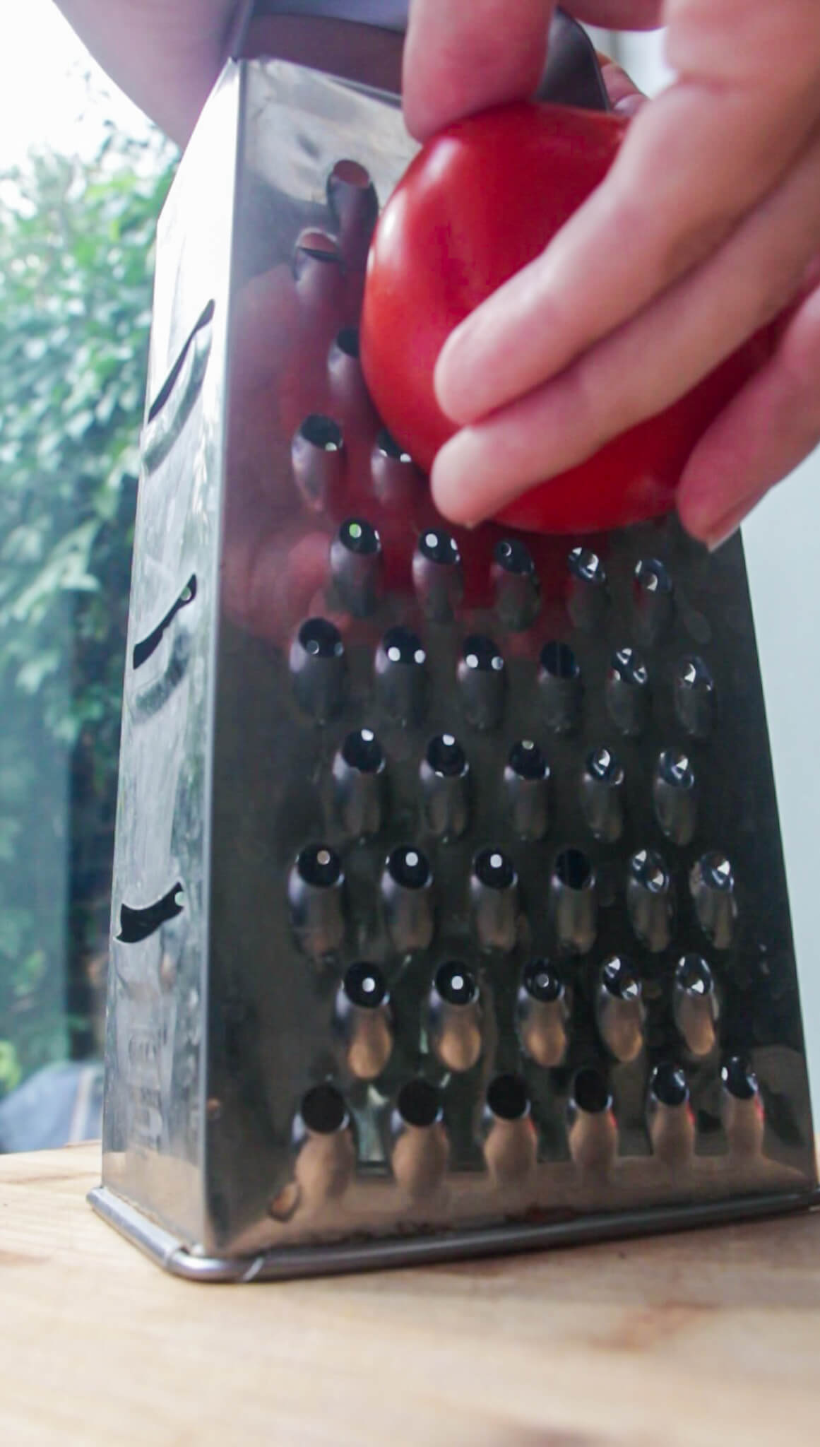 Grating a large tomato on the side of a silver grater.