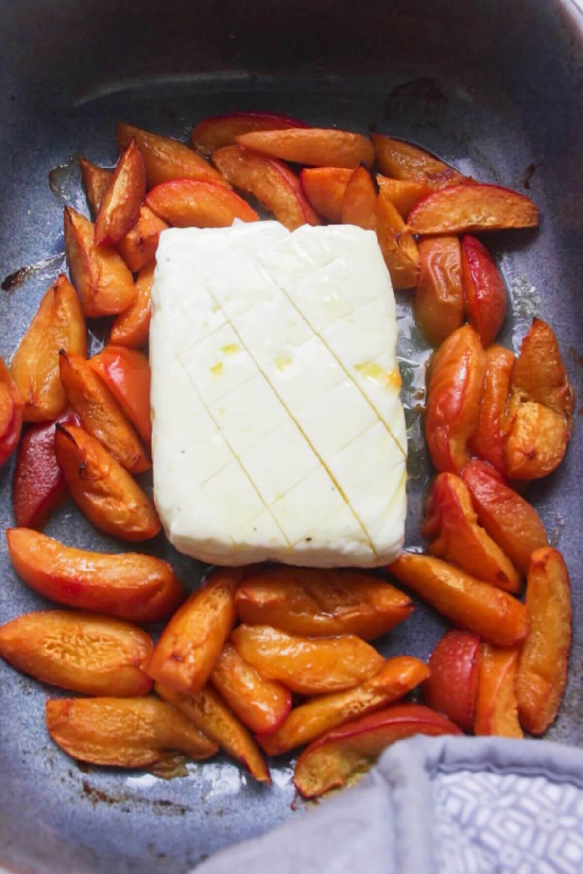 Criss cross cut whole halloumi in the middle of chopped apricots in a small blue oven dish.