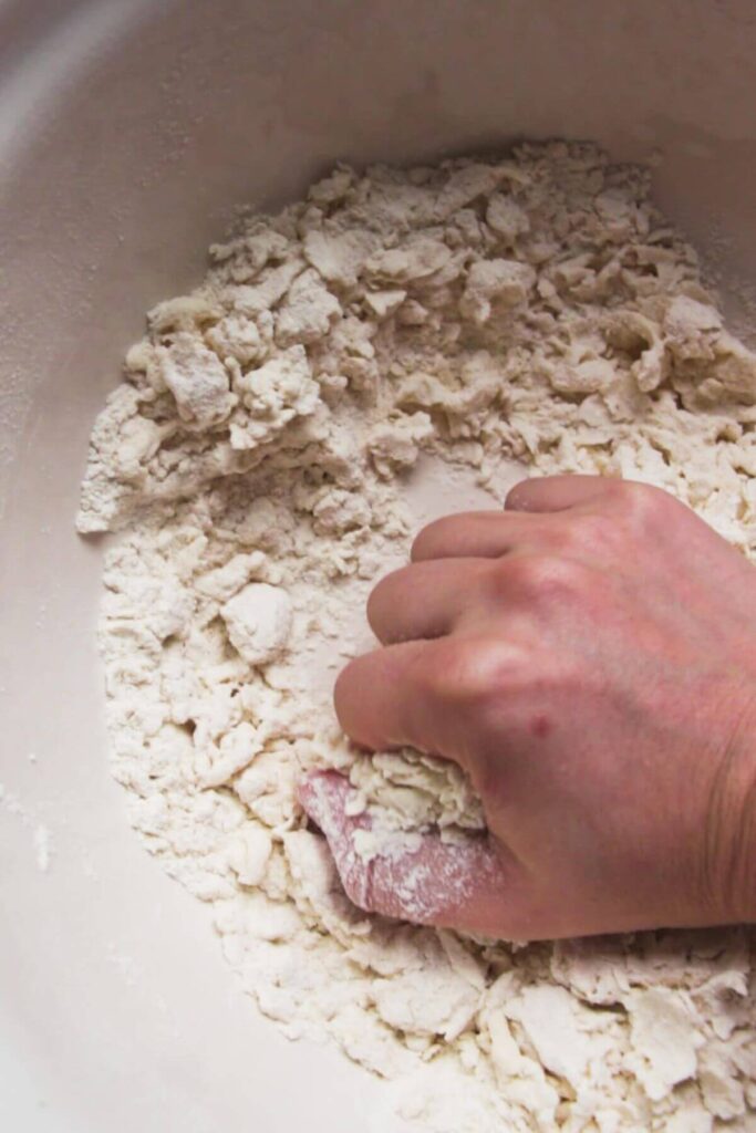 Hand kneading bagel dough in a large white bowl.