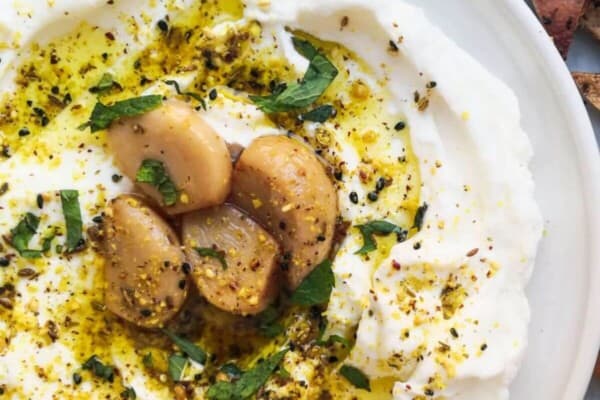 Labneh with confit garlic and dukkah on a plate with pita chips on the side.