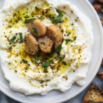 Labneh with confit garlic and dukkah on a plate with pita chips on the side.