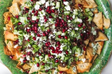 Middle Eastern style nachos on a green plate, with cucumber on the side.