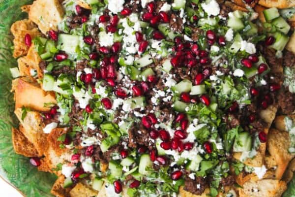 Middle Eastern style nachos on a green plate, with cucumber on the side.