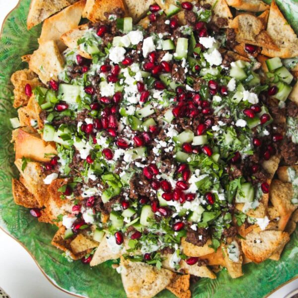 Middle Eastern style nachos on a green plate, with cucumber on the side.