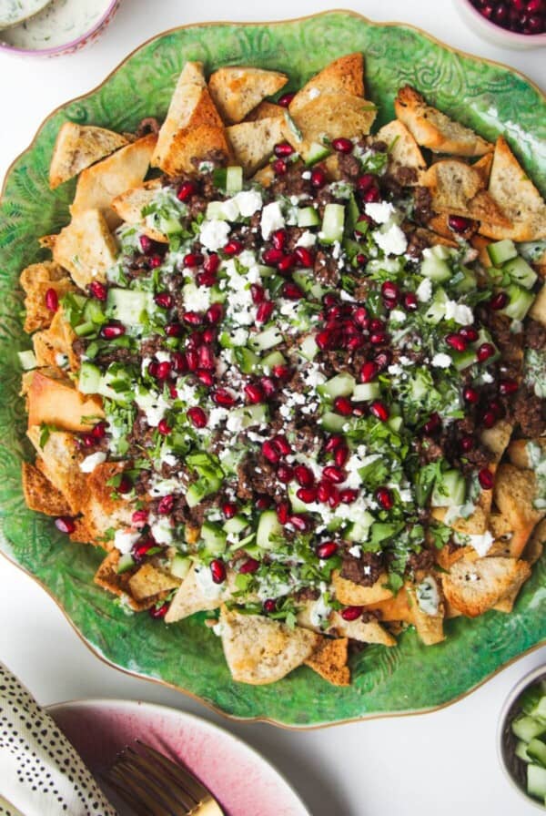 Middle Eastern style nachos on a green plate, with cucumber on the side.