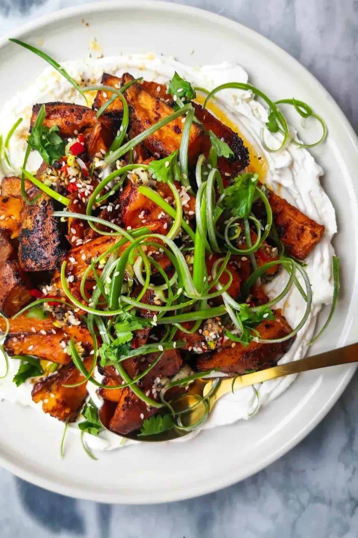 Miso roasted sweet potatoes on labneh, with chilli lime salsa on top on a white plate.