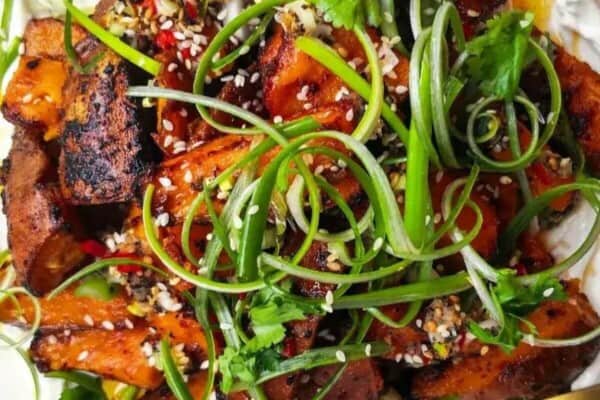 Miso roasted sweet potatoes on labneh, with chilli lime salsa on top on a white plate.