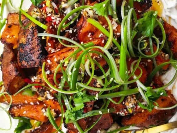 Miso roasted sweet potatoes on labneh, with chilli lime salsa on top on a white plate.