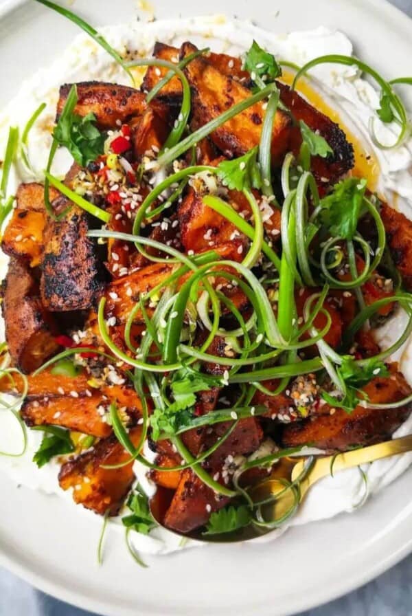 Miso roasted sweet potatoes on labneh, with chilli lime salsa on top on a white plate.