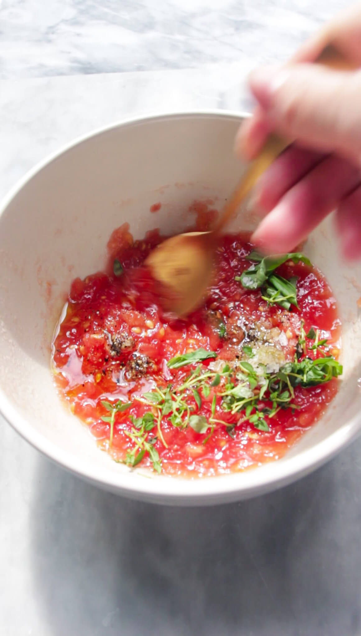Mixing grated tomatoes, thyme, basil, salt and pepper in a small white bowl.