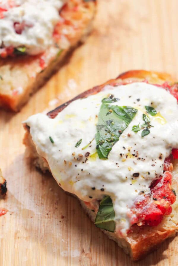Two pieces of pan con tomate with burrate on a wooden board.