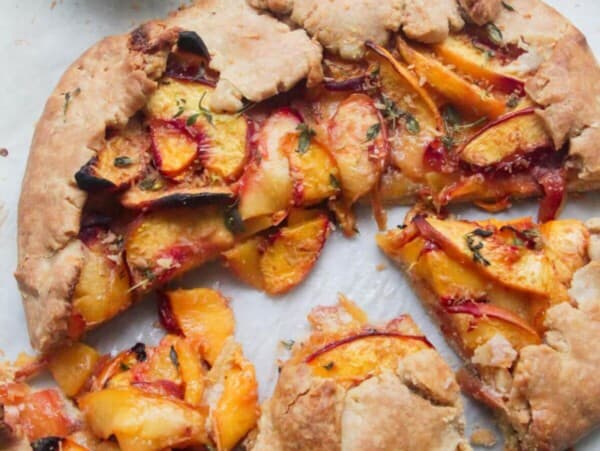 Peach coconut almond galette sliced on a grey marble background with a gold fork.