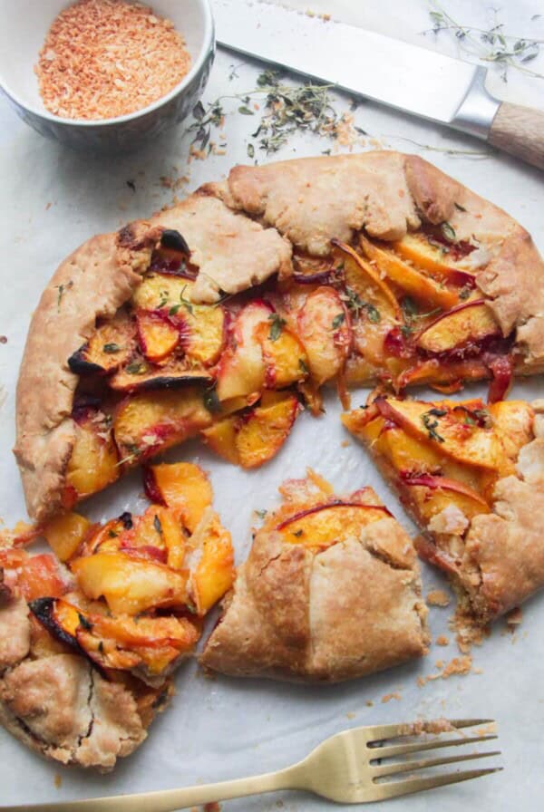 Peach coconut almond galette sliced on a grey marble background with a gold fork.