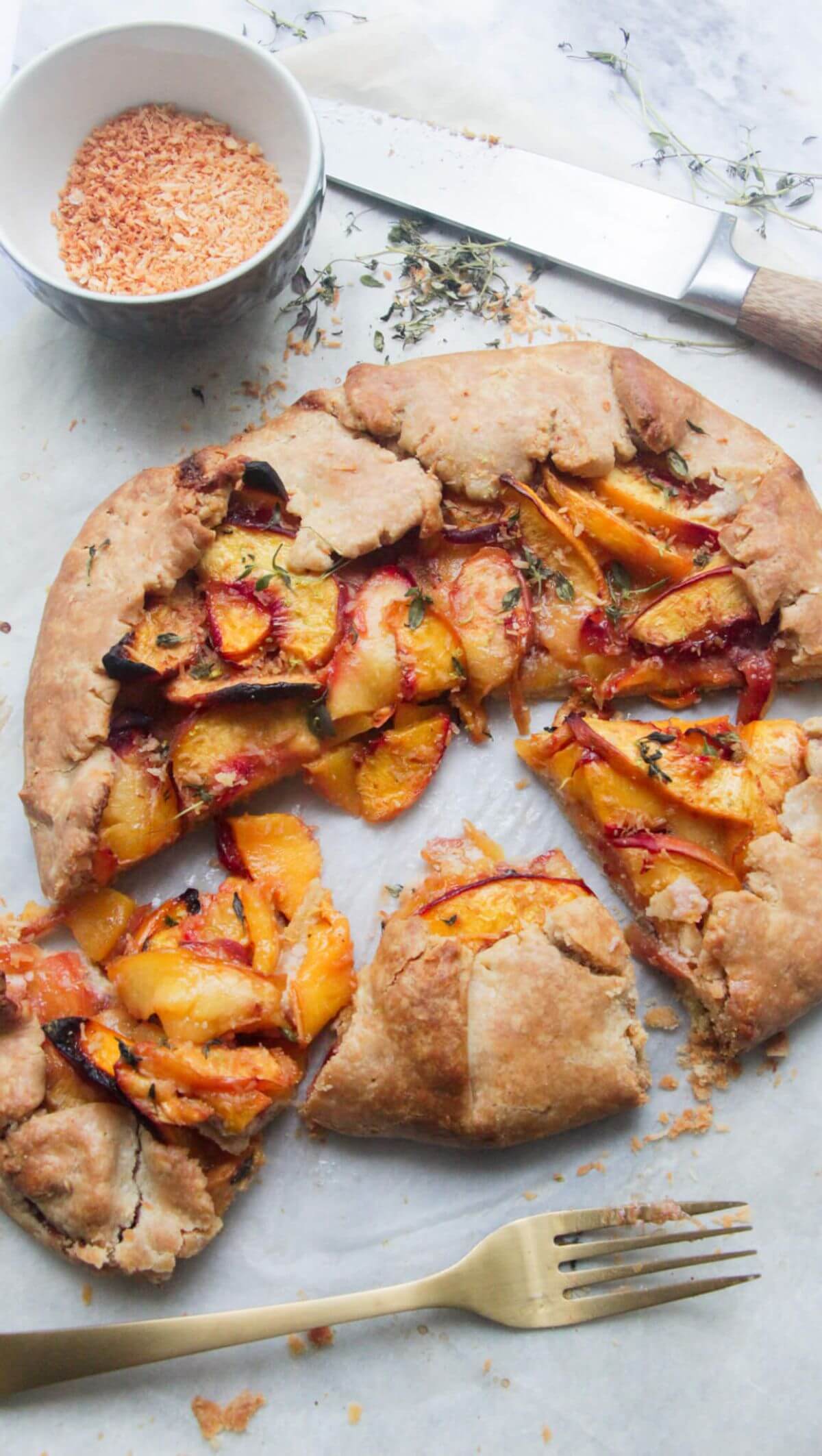 Peach coconut almond galette sliced on a grey marble background with a gold fork.