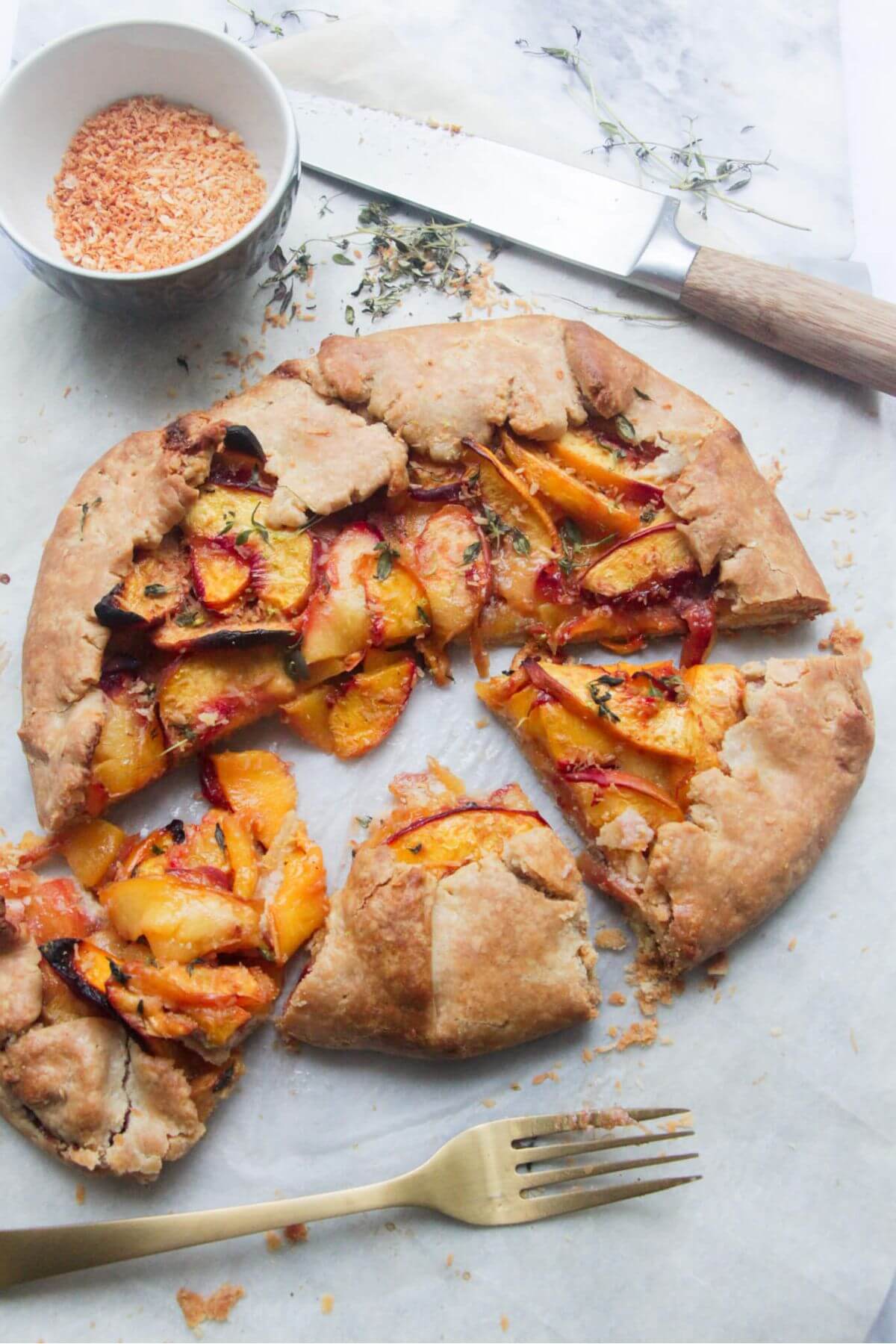Peach almond galette cut into 3 slices with a fork and knife in the background.
