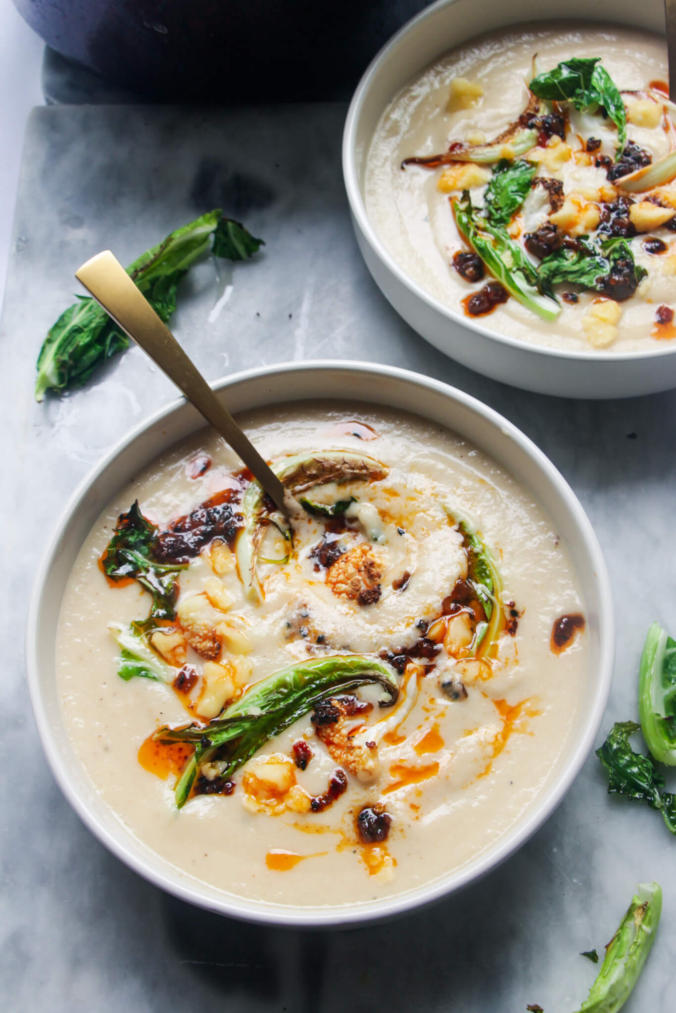 Roasted cauliflower cheese soup in 2 bowls on a grey marble background.