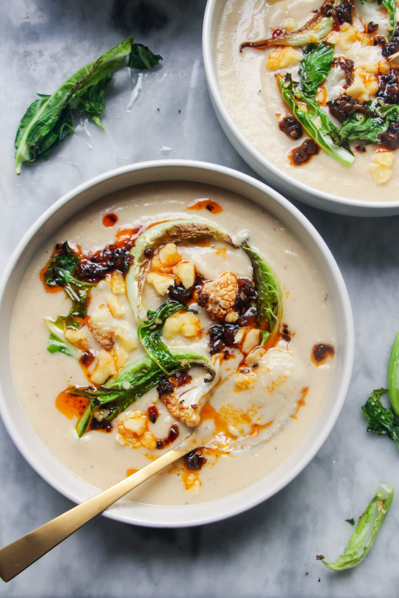 Close up of roasted cauliflower cheese soup in a white bowl with gold spoon inside.
