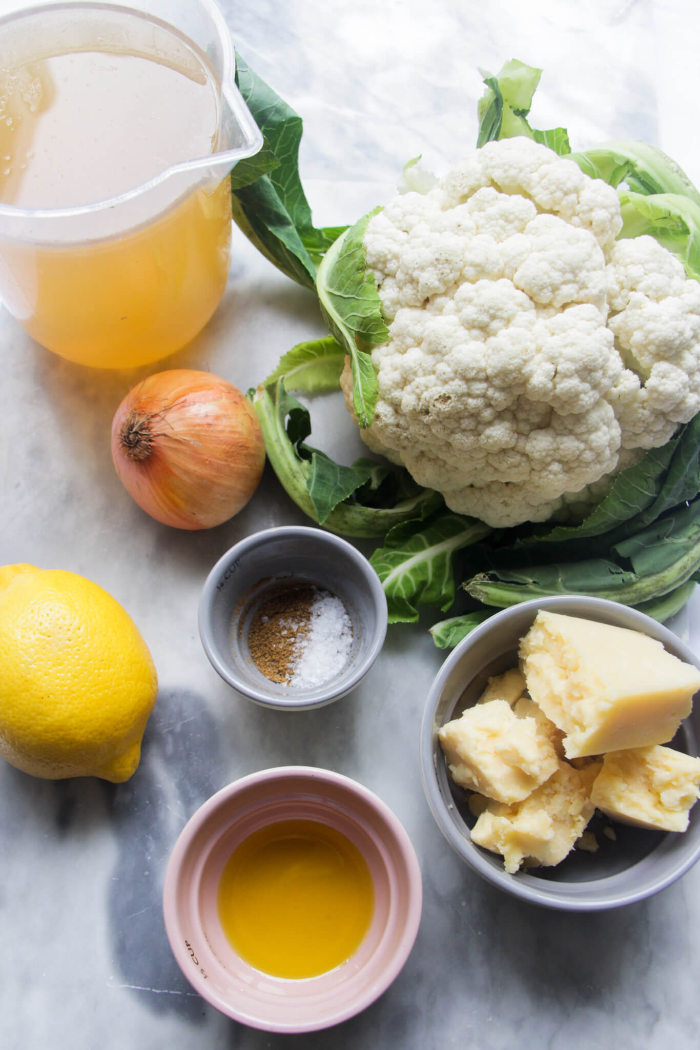 Ingredients for roasted cauliflower cheese soup laid out on a grey marble background.