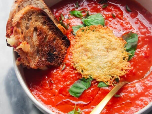 Roasted red pepper and tomato soup in a white bowl with grilled cheese dipped in.