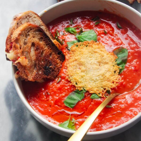 Roasted red pepper and tomato soup in a white bowl with grilled cheese dipped in.