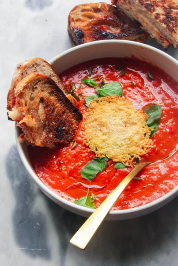 Roasted red pepper and tomato soup in a white bowl with grilled cheese dipped in.