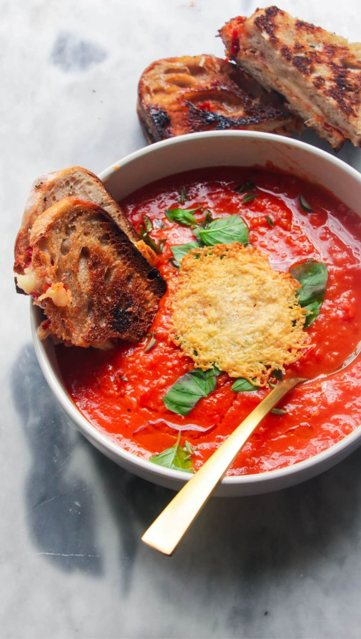 Roasted red pepper and tomato soup in a white bowl with grilled cheese dipped in.