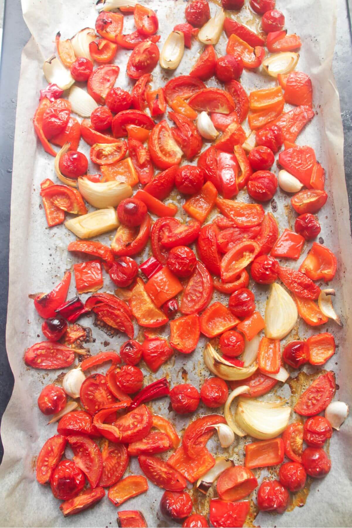 Tomatoes, peppers, onions and garlic roasted on a large lined oven tray.