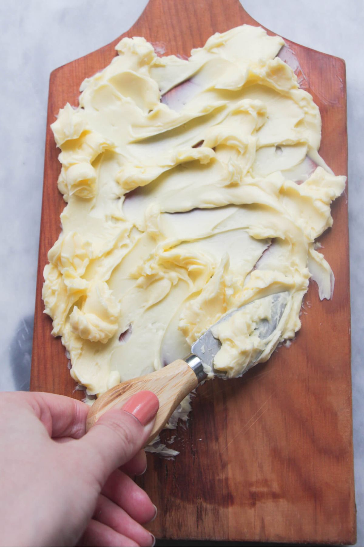 Hand smearing butter onto a board with a small cheese knife.