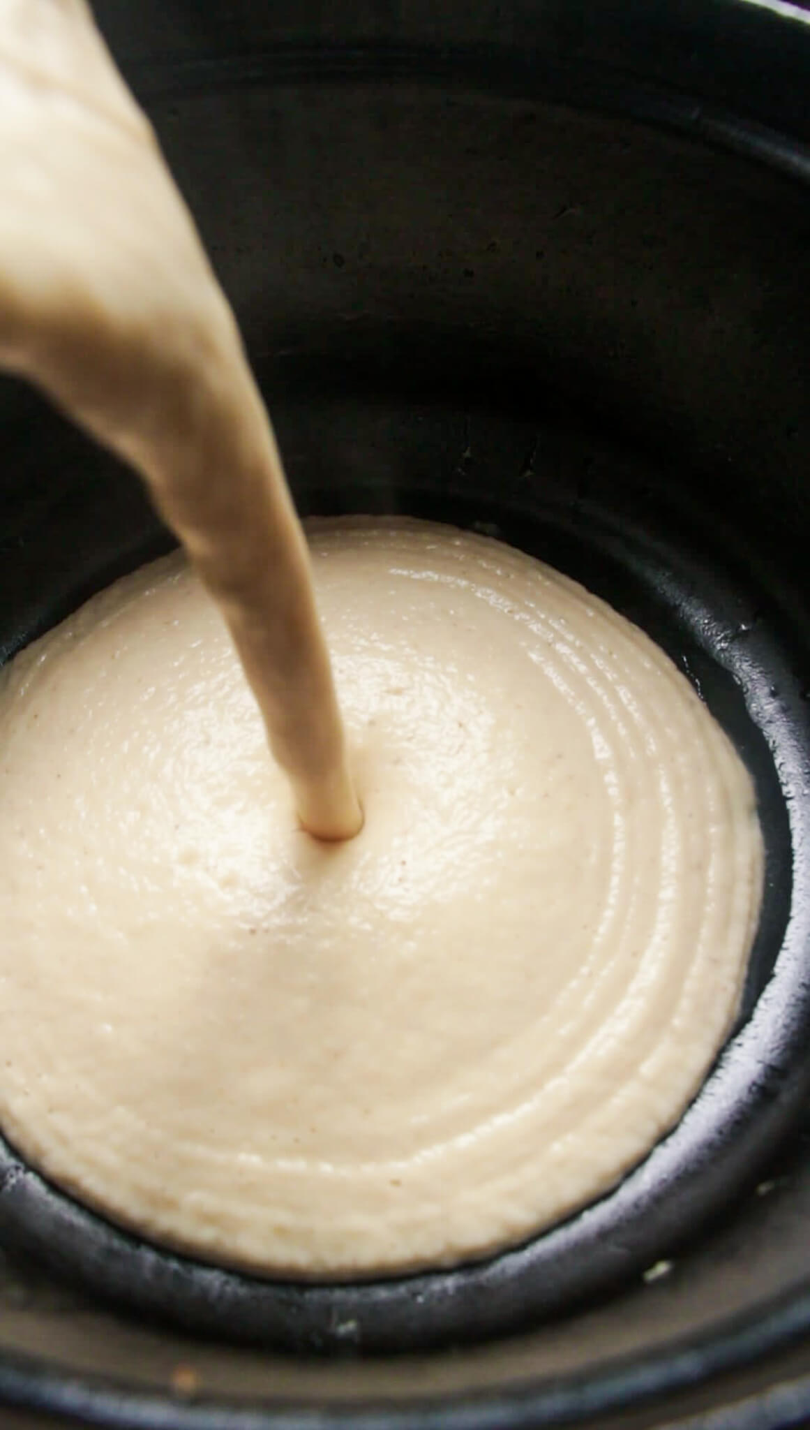 Roasted cauliflower soup being poured from blender into a large pot.