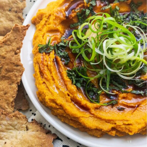 Spiced roasted carrot dip on a white and black patterned background with crackers on the side.