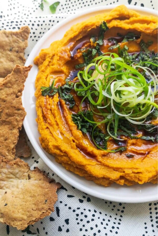 Spiced roasted carrot dip on a white and black patterned background with crackers on the side.