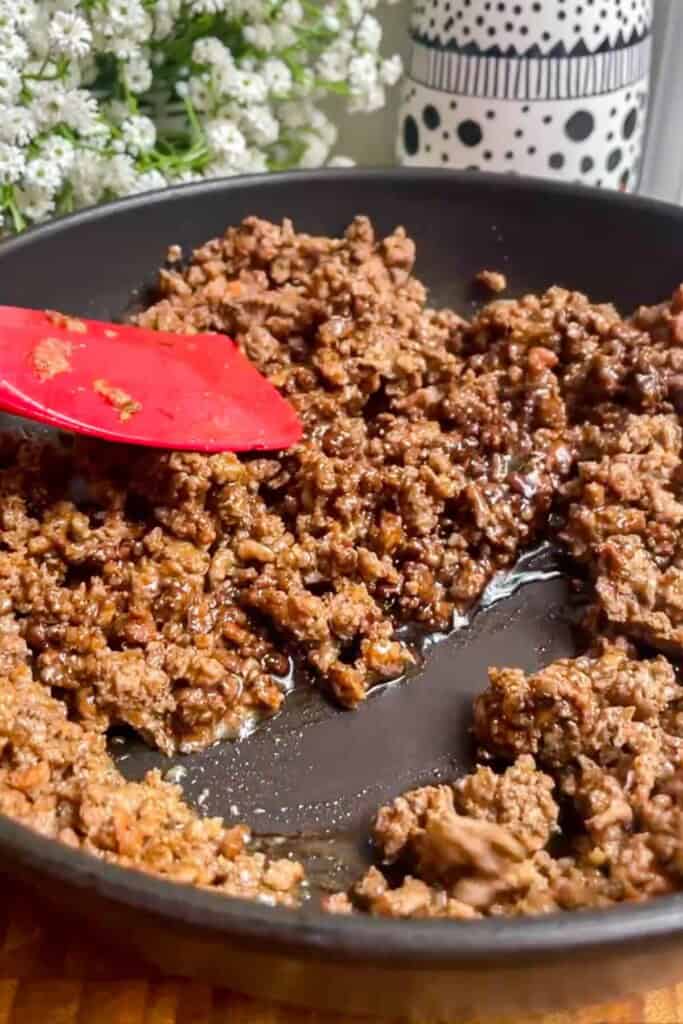 Spatula stirring sticky ground beef in a pan.