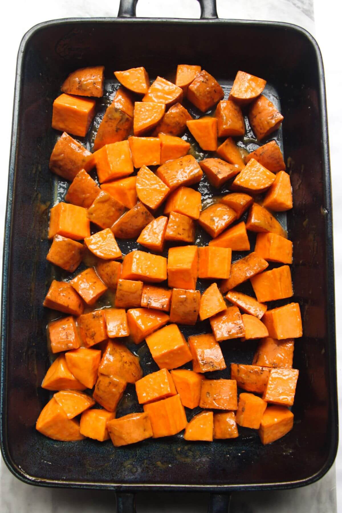 Miso glazed sweet potato chunks in a large blue oven dish ready to be roasted.