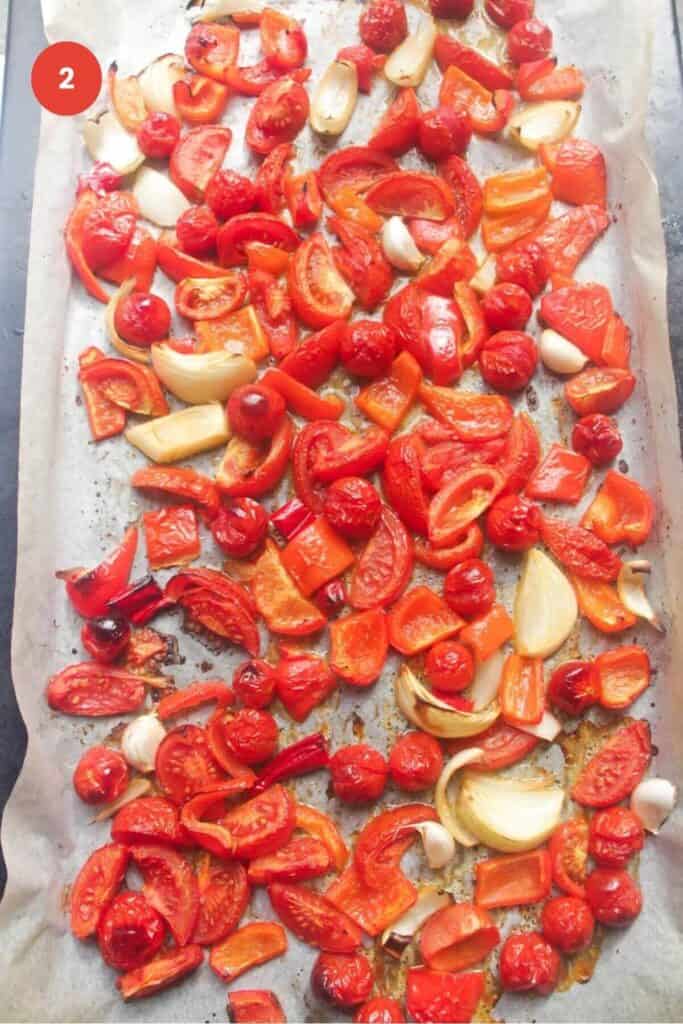 Roasted tomatoes, bell peppers, garlic and onion on a baking sheet.