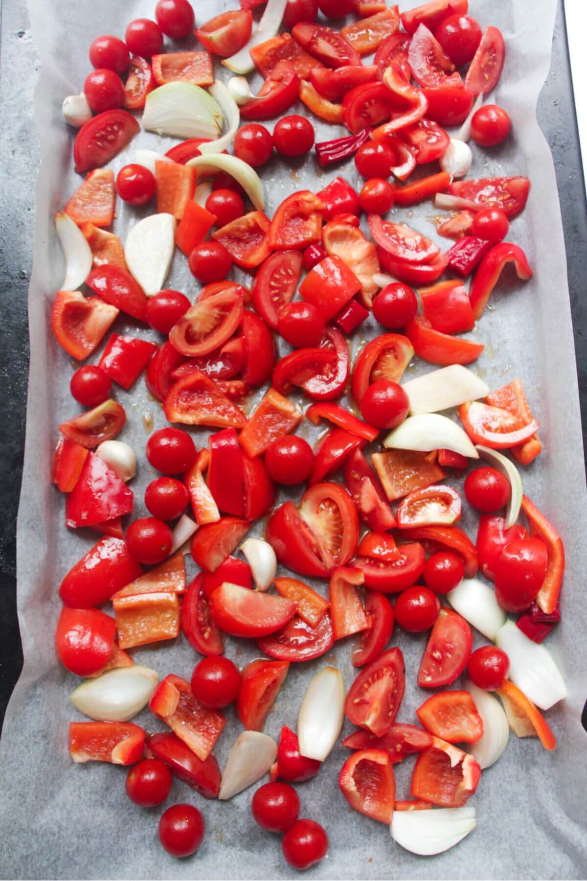 Chopped tomatoes, red pepper, onion and garlic laid out on a large lined oven tray.