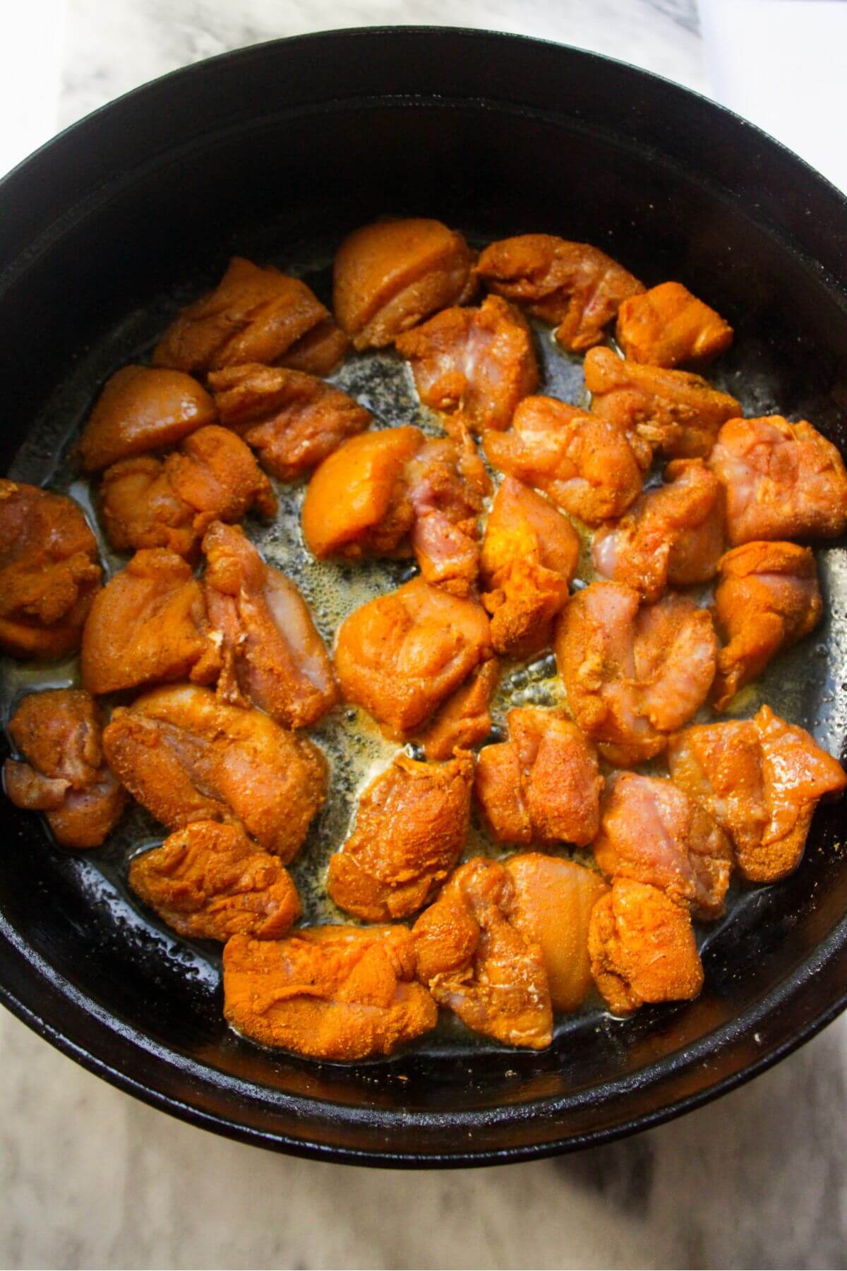 Chopped chicken thighs cooking in a large black pan.