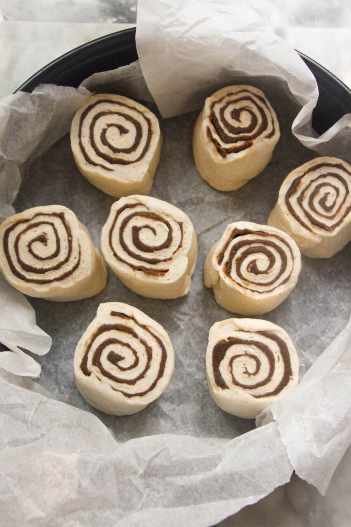 Pumpkin spice cinnamon rolls in baking paper lined cake tin ready to be baked.