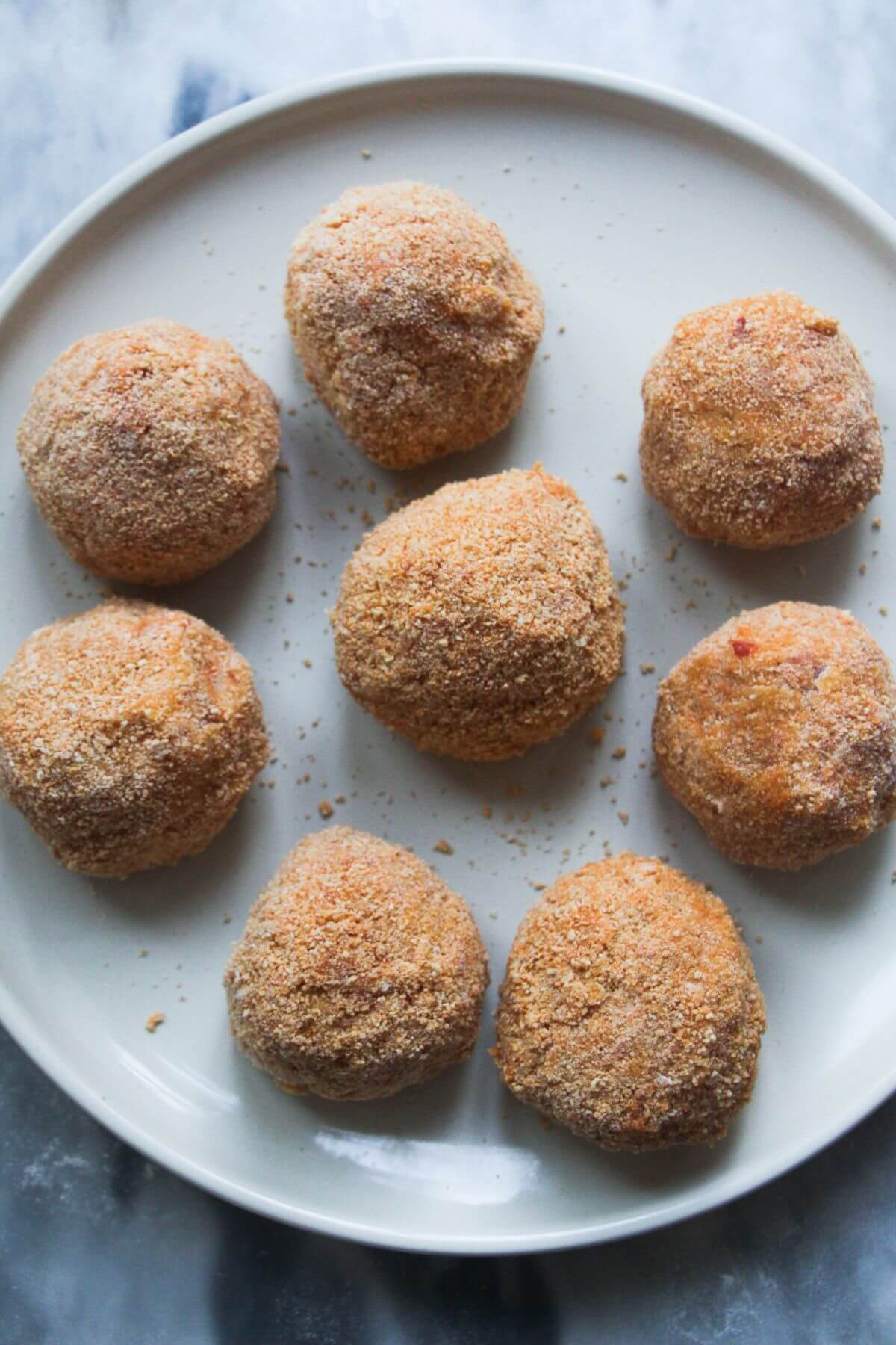 8 coated arancini balls pre frying, on a large white plate.