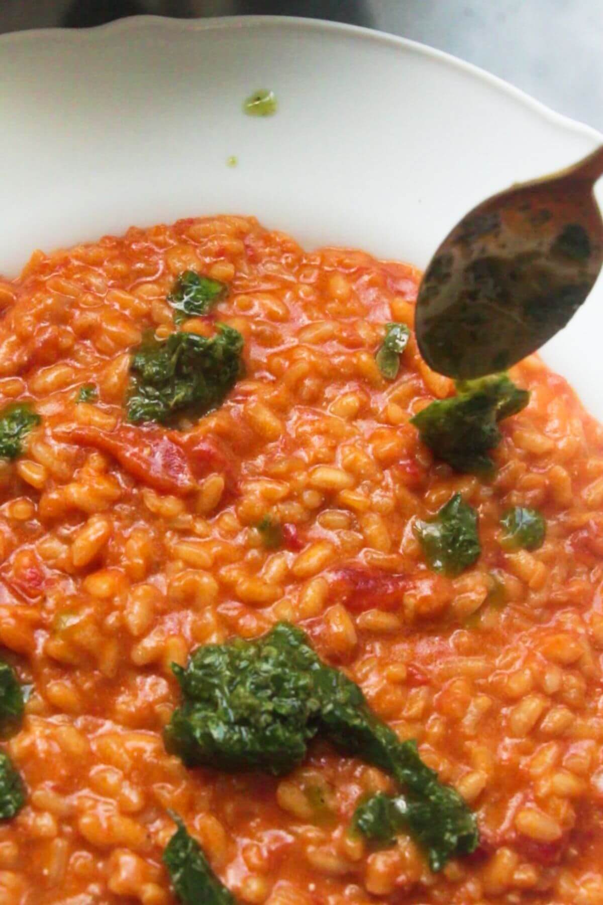 Small gold spoon topping tomato risotto with green basil pesto.