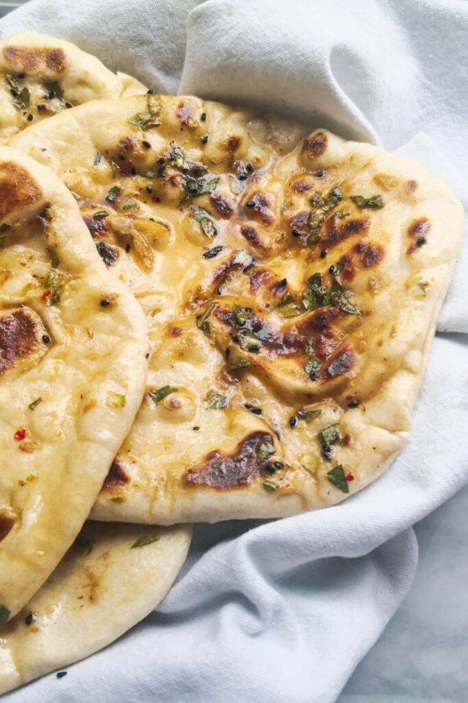 Close up of a pile of garlic naan breads in a white tea towel.