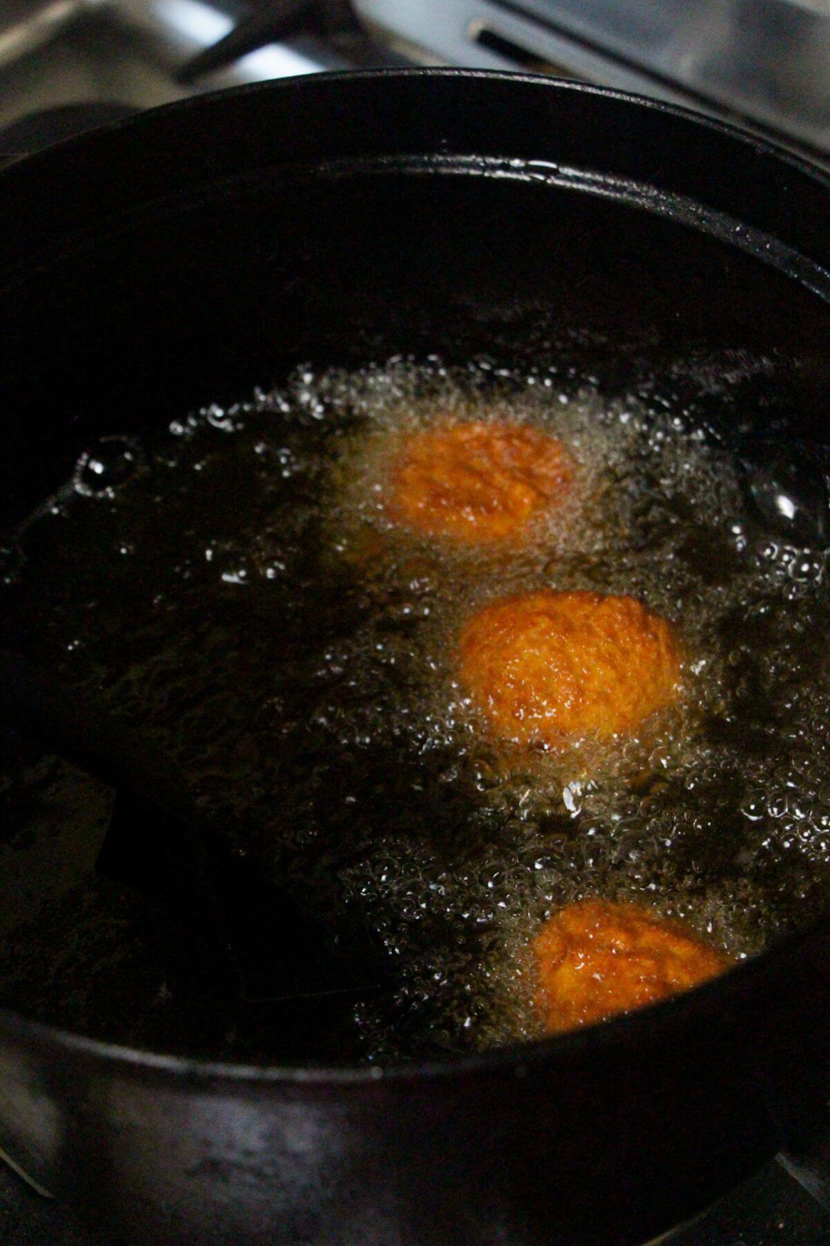 3 arancini balls frying in oil in a large black pot.