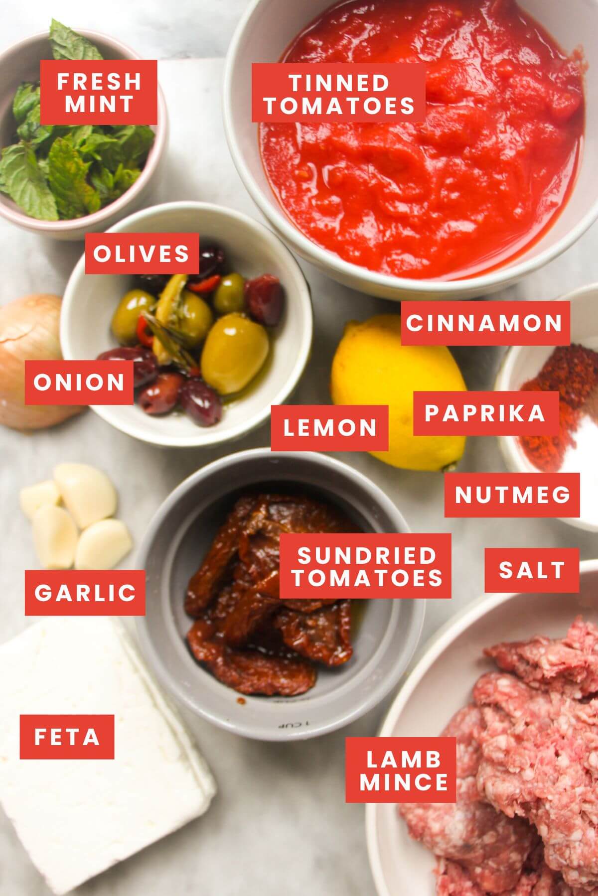 Ingredients for baked Greek meatballs laid out on a grey marble background and labelled.