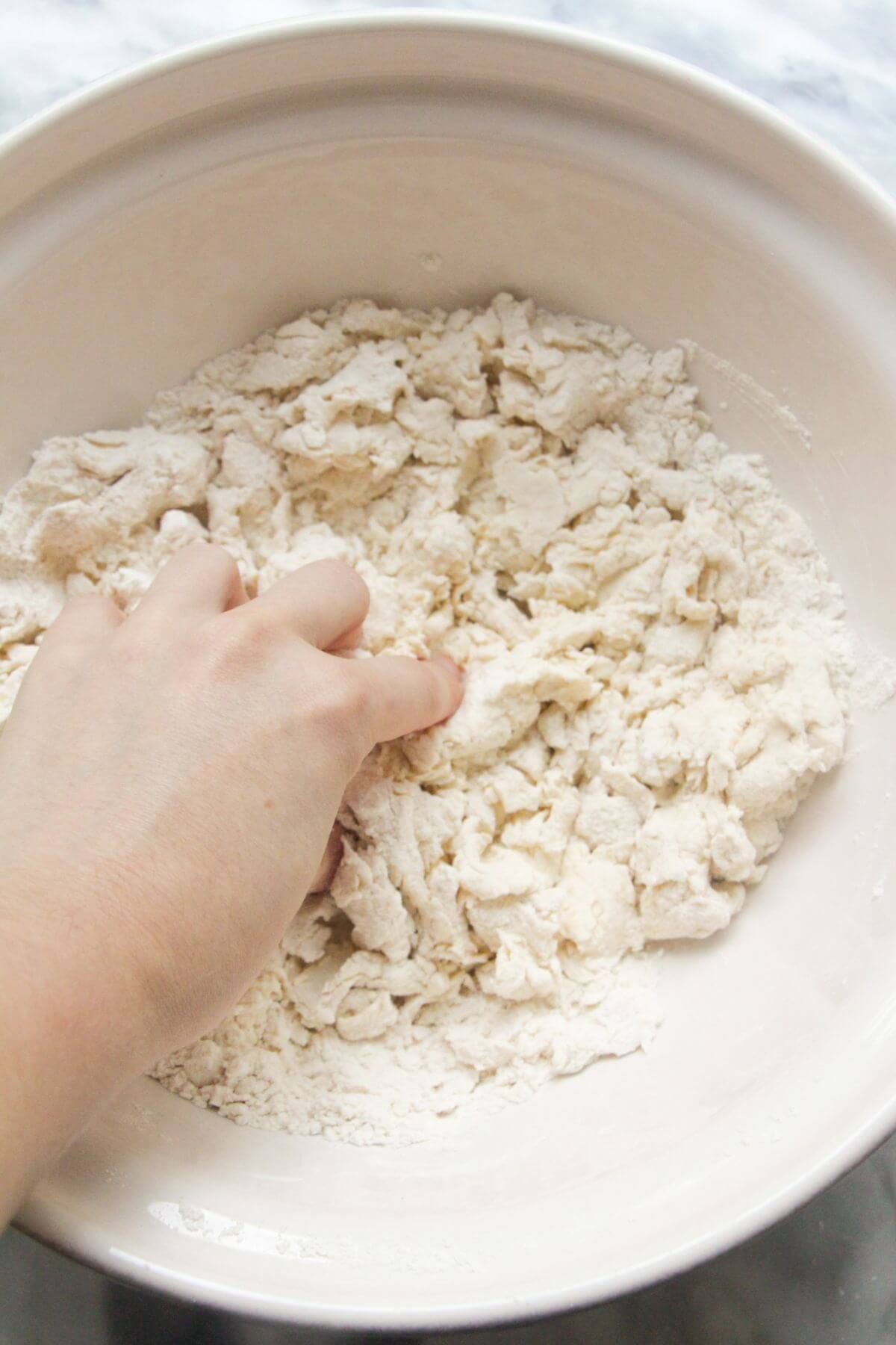Hand scrunching up flour and yogurt in a large bowl to form a dough.