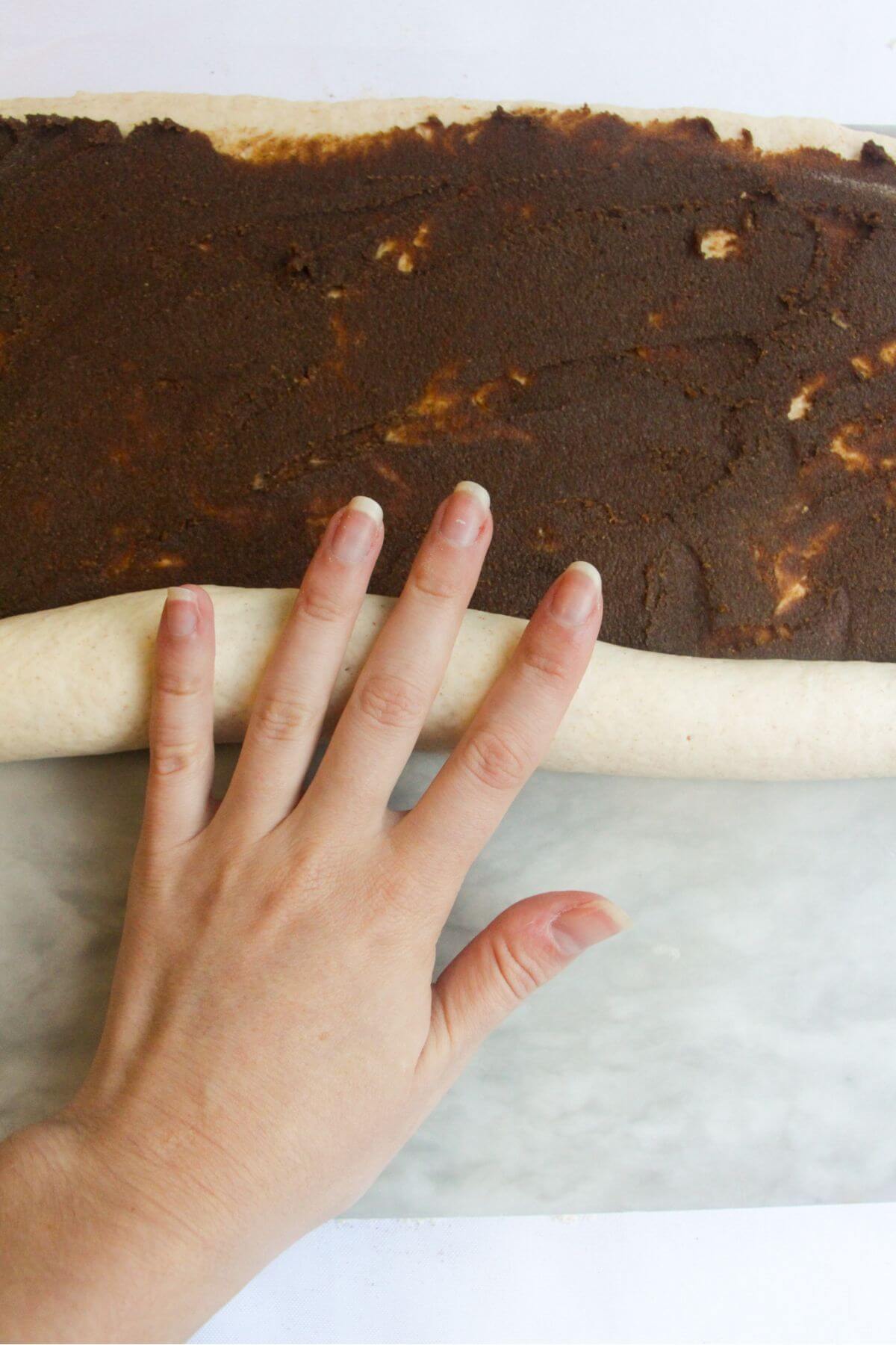 Hand rolling up pumpkin spice butter spread dough into a long log.