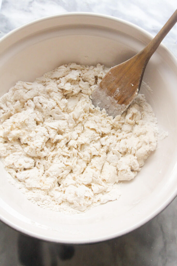 Wooden spatula in a large white bowl with crumbly yogurt and flour mixture.