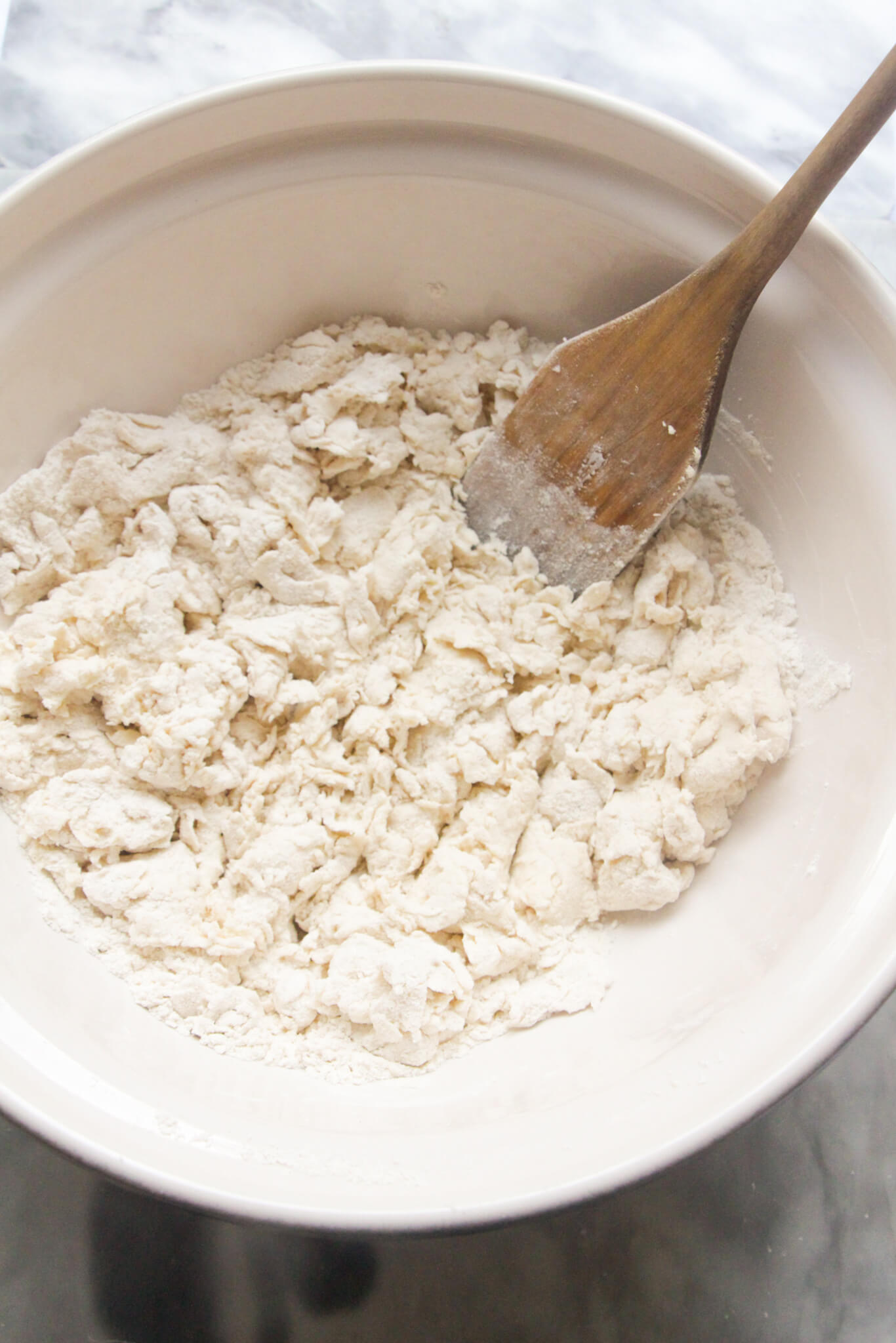 Lumpy mixed flour and yogurt dough in a large white mixing bowl with a wooden spatula inside.