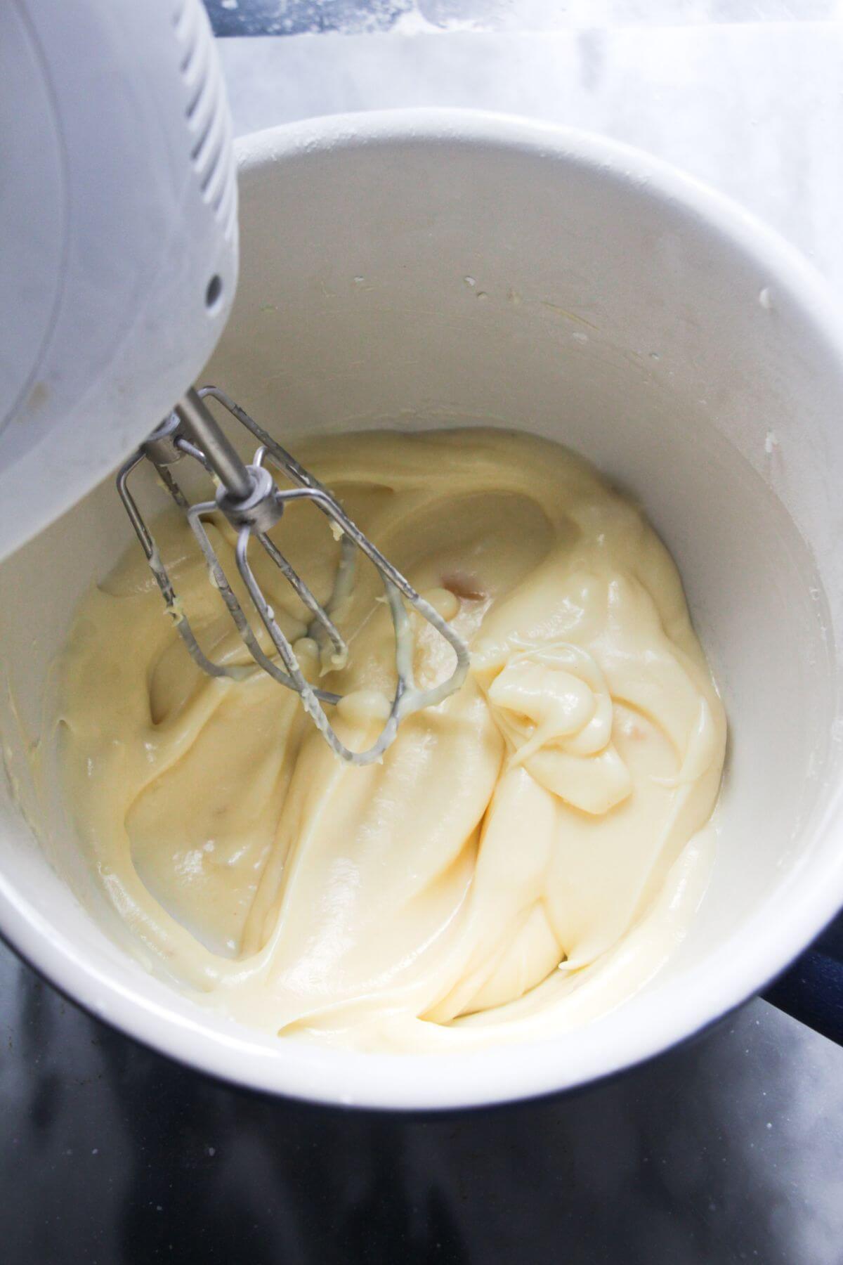 Electric whisk in a bowl with cream cheese ginger icing.