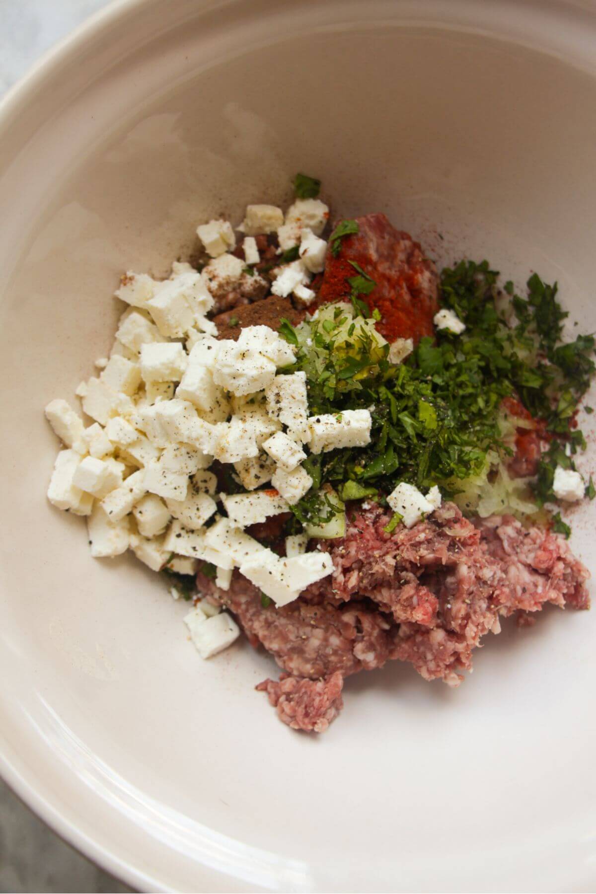 Lamb mince, feta, herbs, spices in a large white mixing bowl.