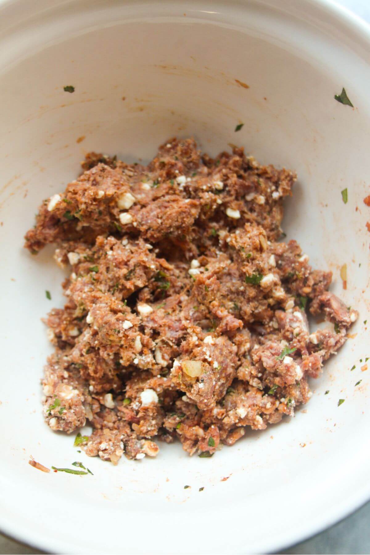 Lamb mince mixed with feta, spices, onion in a large white mixing bowl.
